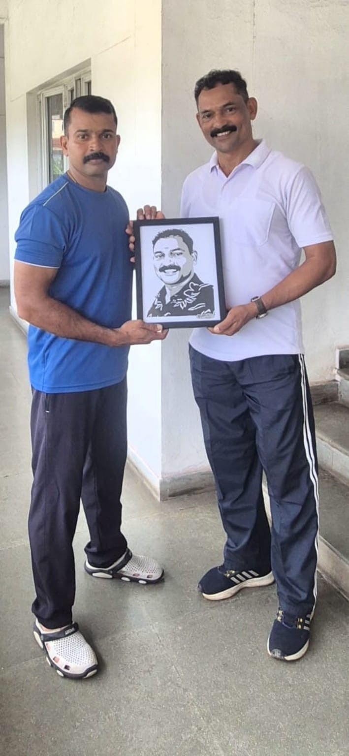 Two men standing together with a framed paper-cut portrait of a smiling man in a floral shirt